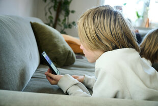 Ein Junge liegt auf einem Sofa und guckt auf sein Smartphone.