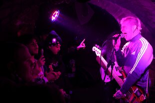 Ein Sänger in Sportjacke mit Gitarre schreit ins Mikro
