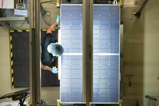 Eine Mitarbeiterin mit tätowierten ARmen steht über Solamodulen in der Produktion