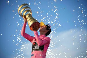 Simon Yates reckt im rosa Trikot die Trophäe in den blauen Himmel