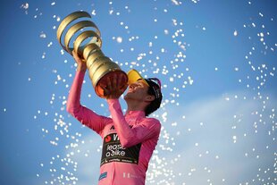 Simon Yates reckt im rosa Trikot die Trophäe in den blauen Himmel
