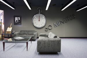 Eine riesige Uhr im Taschenuhrformat, daneben ein Porträt , davor Couch und Beistelltisch