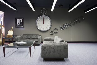 Eine riesige Uhr im Taschenuhrformat, daneben ein Porträt , davor Couch und Beistelltisch