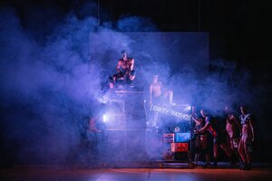 Eine Gruppe Männer mit nackten Oberkörpern versammelt um Musikboxen und Bierkästen