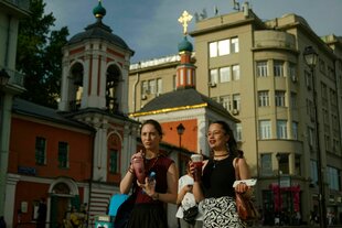 zwei sommerlich gekleidete Frauen haben eine Getränk in der Hand und spazieren über eine russische Strasse