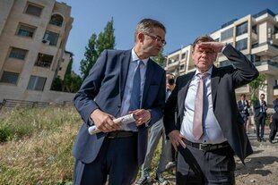 Wadephul hebt die Hand über die Augen, neben ihm steht ein Mann in einer Siedlung