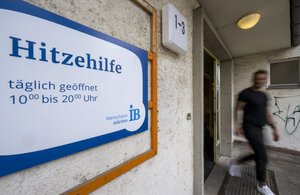 Eine Tafel mit Informationen zu den Öffnungszeiten hängt am Eingang zu der Notunterkunft der Hitzehilfe für wohnungs- und obdachlose Menschen im Bezirk Schöneberg. Die erste Sommer-Notunterkunft Berlins wird in Zusammenarbeit mit Internationalem Bund (IB)