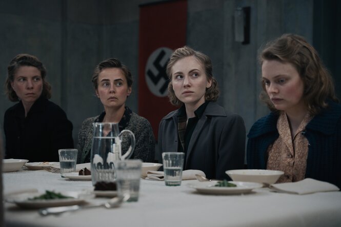 Vier Frauen – die Vorkosterinnen – sitzen an einer weißen Tafel und blicken unglücklich.
