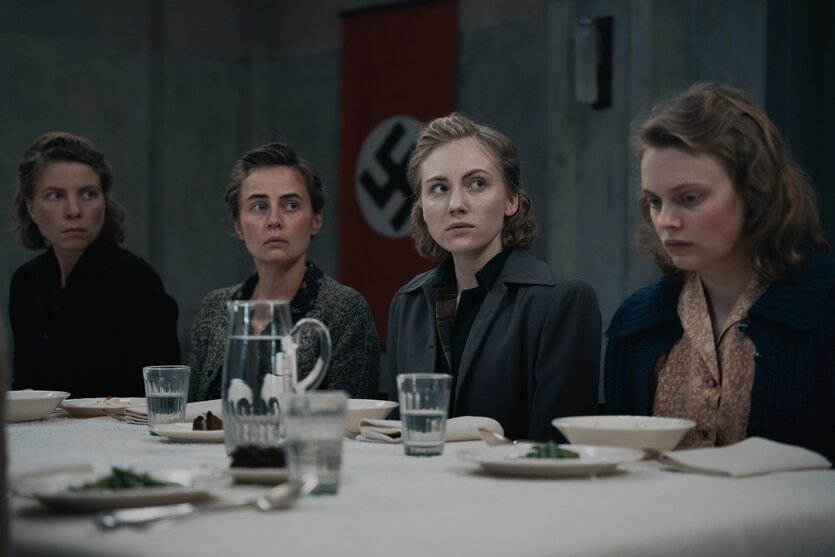 Vier Frauen – die Vorkosterinnen – sitzen an einer weißen Tafel und blicken unglücklich.