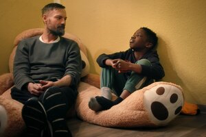 Ein Kind und ein Mann sitzen auf einem Riesenkuscheltier und schauen sich schweigend an