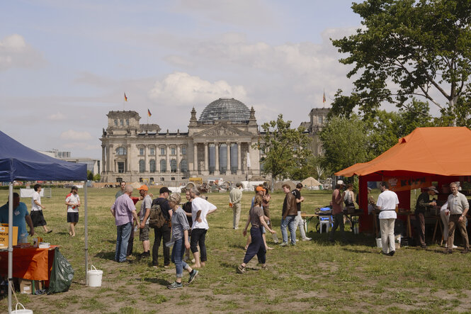 Zelte auf der Wiese vor dem Bundestag. vor dem sich Menschen tummeln