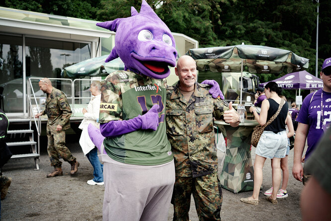 Ein Mensch, der in ein Plüschtier-Kostüm gekleidet ist und ein Bundesewehrsoldat in Tarnfleck-Uniform, der den Daumen hoch hält
