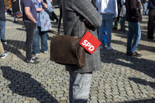 Ein Mensch in karriertem Jacket und mit Ledertasche, in der ein SPD-Fähnchen steckt