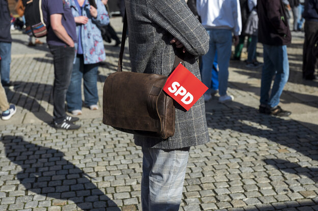 Ein Mensch in karriertem Jacket und mit Ledertasche, in der ein SPD-Fähnchen steckt