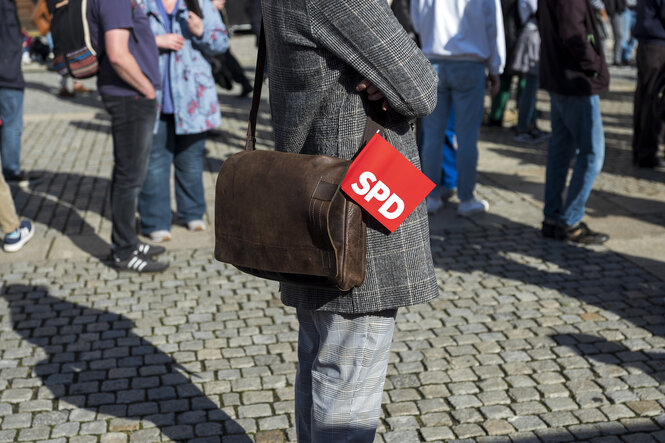 Ein Mensch in karriertem Jacket und mit Ledertasche, in der ein SPD-Fähnchen steckt