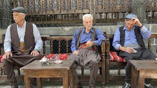 Drei Männer sitzen auf einer Bank und trinken Tee