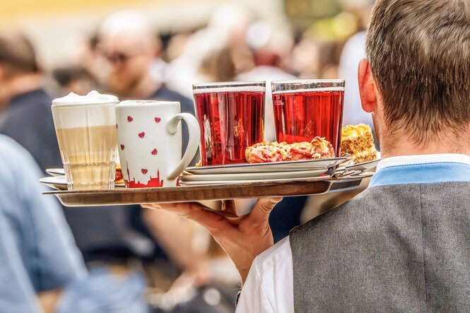 Kellner von hinten mit einem Tablett ,beladen mit Kaffee Kuchen