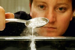 Eine Frau gießt mit einem Löffel flüssiges Blei in Wasser.