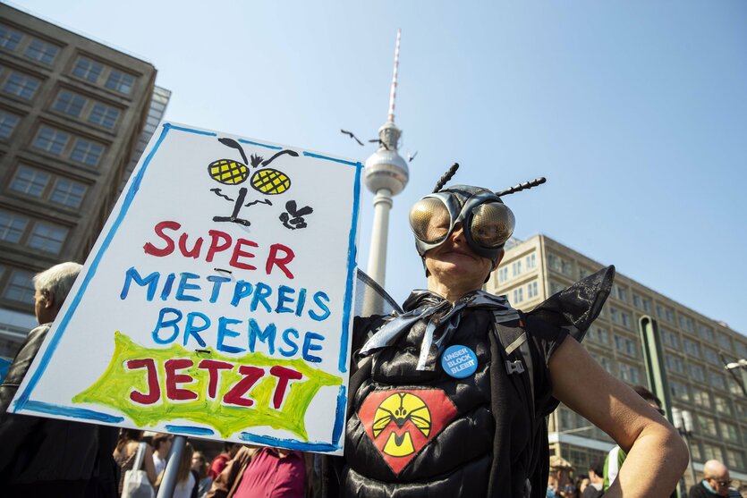 Ein Mensch in einem Kostüm fordert auf einem Plakat "Super Mietpreisbremse jetzt"