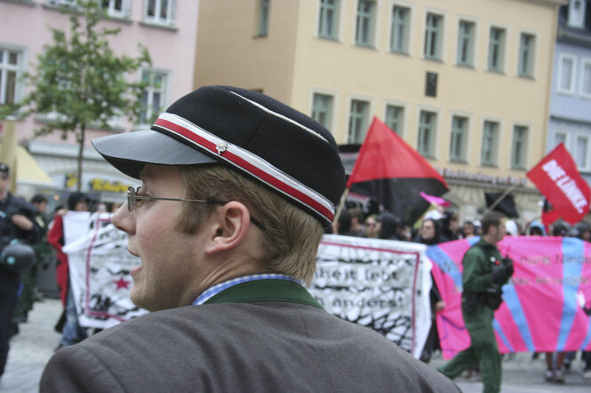 Zwei Mitglieder von Studentenverbindungen schauen belustigt auf Demonstranten und trinken dabei Bier