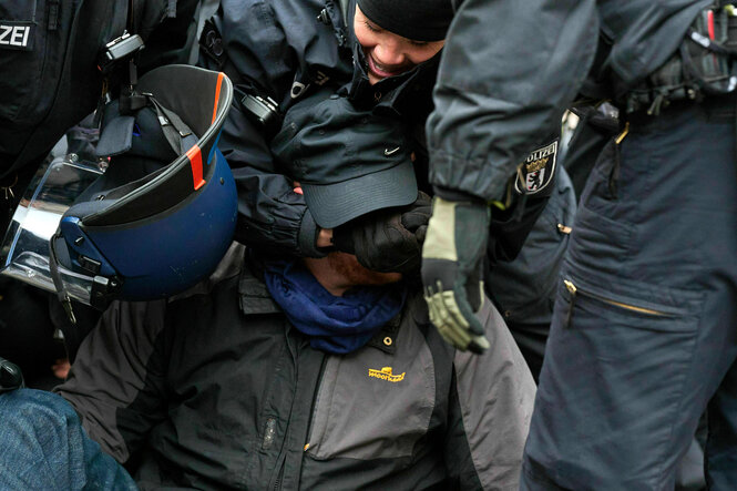 Polizisten beuegen sich über einen Mann, einer fasst ihm ins Gesicht was ihn sehr zu freuen scheint