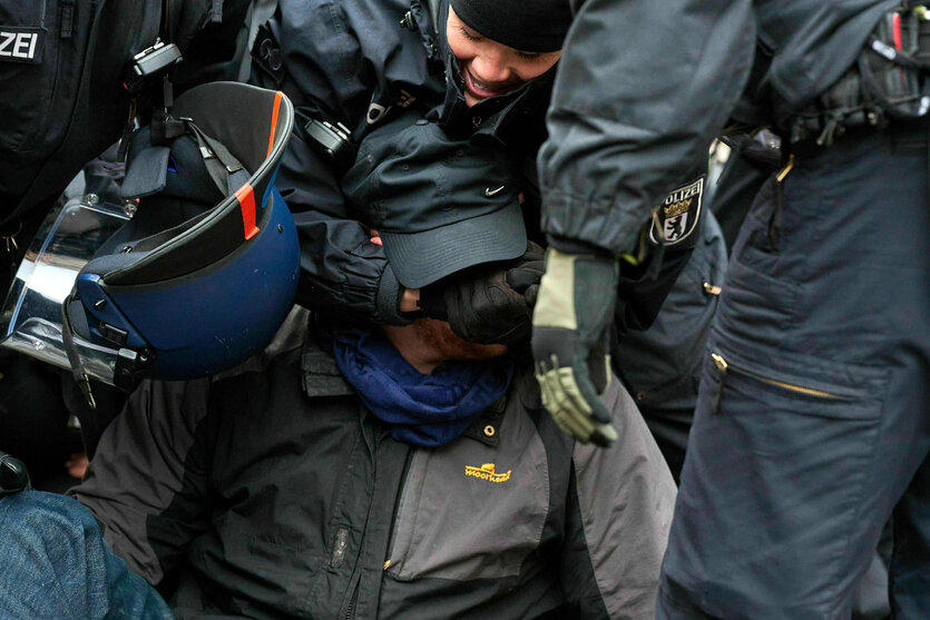 Polizisten beuegen sich über einen Mann, einer fasst ihm ins Gesicht was ihn sehr zu freuen scheint