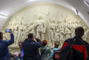 Zu sehen ist ein sovjetisches Relief mit Stalin und Besucher der Sehenswürdigkeit.