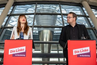 Heidi Reichinnek und Sören Pellmann stehen hinter Stehpulten mit der Aufschrift 