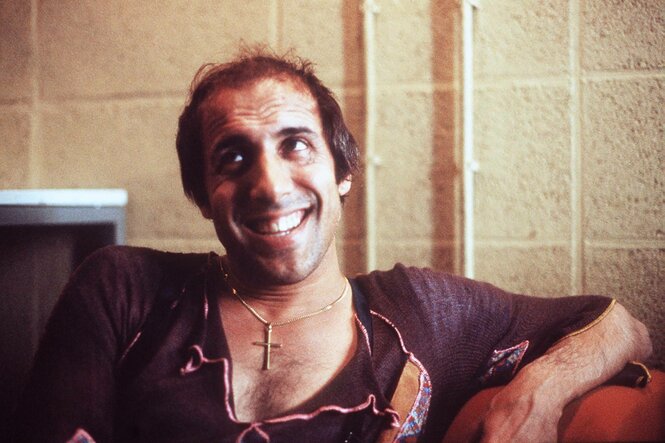 Adriano Celentano mit entblößter brust und Kreuz auf der Brust, verschmitzt lächelnd