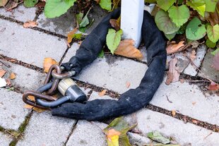 EIn dickes Fahrschloss liegt auf dem Boden an einen Pfosten gekettet