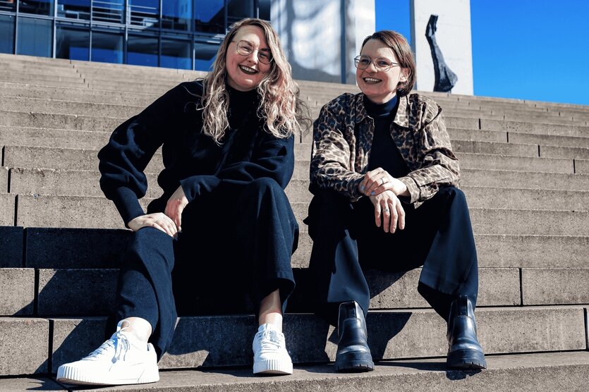 Zwei junge Frauen sitzen auf einer Treppe und lachen