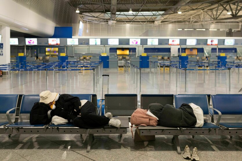Zwei Passagiere schlafen auf einer FLughafenbank, der Flughafen scheint ausgestorben und leer.