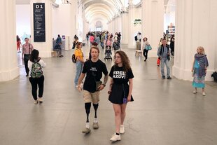 Ein junger Mann mit zwei Beinprothesen und seine Begleiterin, die ein T-shirt trägt mit der Aufschrift "Free Azov" auf einer Buchmesse in Kyiv