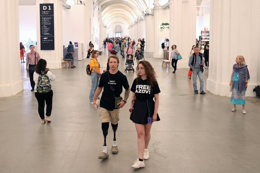 Ein junger Mann mit zwei Beinprothesen und seine Begleiterin, die ein T-shirt trägt mit der Aufschrift "Free Azov" auf einer Buchmesse in Kyiv