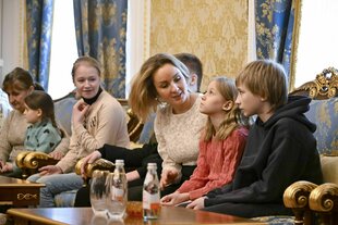 Maria Lvova-Belova (Mitte) sitzt mit Kindern, die einen nachdenklichen Eindruck machen auf einem Sofa