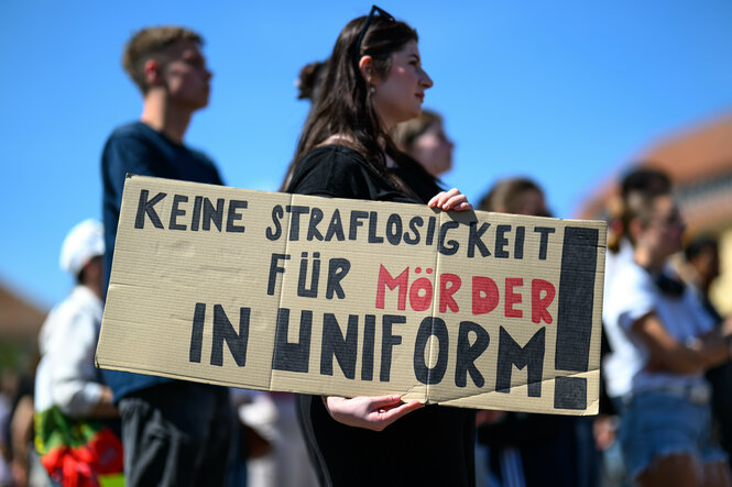 Eine Frau hält auf deiner Demonstration ein Schild hoch, auf dem steht: Keine Straflosigkeit für Mörder in Uniform