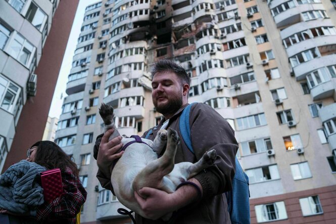 Ein Mann trägt seinen Hund vor einem von russischen Drohnen zerstörten Wohnhaus in Kyjiw