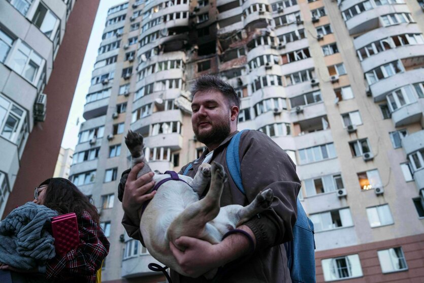 Ein Mann trägt seinen Hund vor einem von russischen Drohnen zerstörten Wohnhaus in Kyjiw