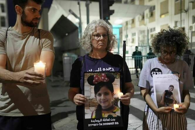 Menschen stehen mit ernsten Gesichtern in Tel Aviv auf der Straße, ein Mann hält eine brennende Kerze, die beiden Frauen zeigen Fotos von getöteten Kindern aus Gaza