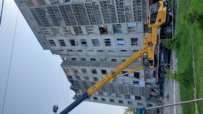 Ein Kran steht vor einem Plattenbau, dessen obere Stockwerke von den Raketen getroffen und beschädigt wurden