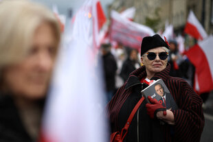 Eine Teilnehmerin schick gekleidet mit Mütze und Sonnenbrille bei einer Demonstration gegen Einwanderer in Warschau. Sie hält ein Buch inder Hand das den neuen Präsidenten Karol Nawrocki zeigt