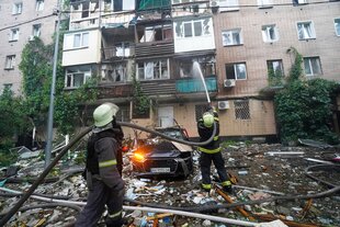 Mehrere Feuerwehrmänner stehen vor einem beschädigten Haus