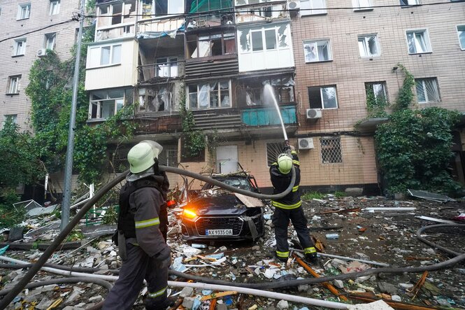 Mehrere Feuerwehrmänner stehen vor einem beschädigten Haus