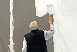 Ein älterer Mann mit grauen Haaren streicht eine Wand