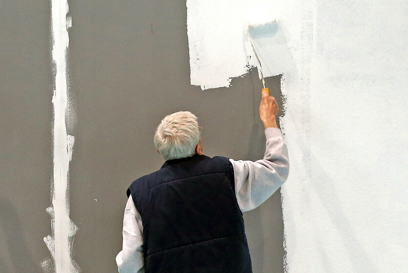 Ein älterer Mann mit grauen Haaren streicht eine Wand