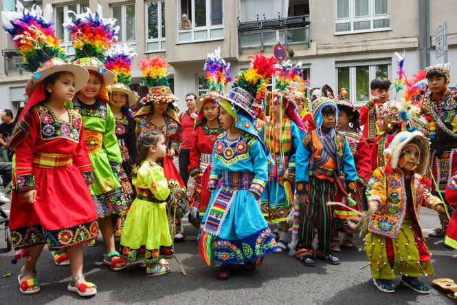 Kinder in bunten, traditionellen Kostümen laufen durch eine Straße