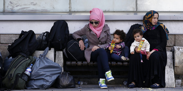 Zwei syrische Frauen mit zwei Kindern und Gepäck sitzen auf einer Bank in Istanbul