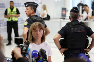 Eine junge Frau spricht mit Vertretern der Presse, während Polizisten die Situation bewachen