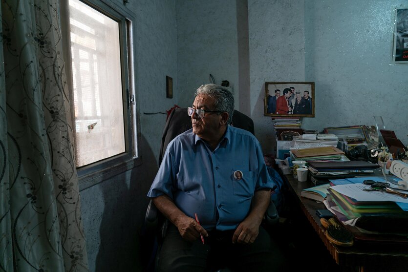 Ali Samoudi sitzt an seinem Schreibtisch mit vielen Akten und Papieren, er schaut aus einem kleinen Fenster