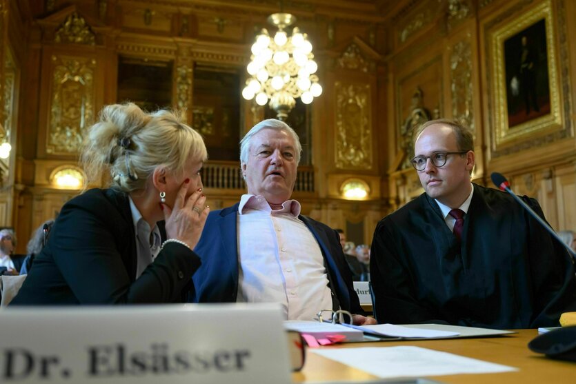 Drei Personen sitzen auf der Anklagebank und sprechen miteinander